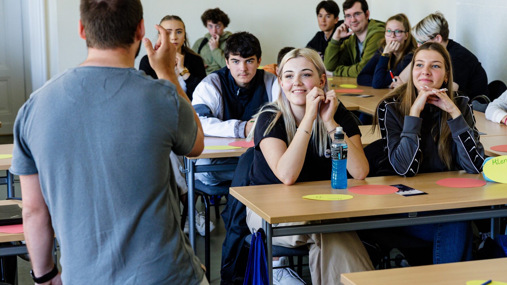 Auf dem Foto ist eine Schulklasse aus Sicht des Lehrer zu sehen. Auf den Tischen der Schüler*innen sind Workshopmaterialien.