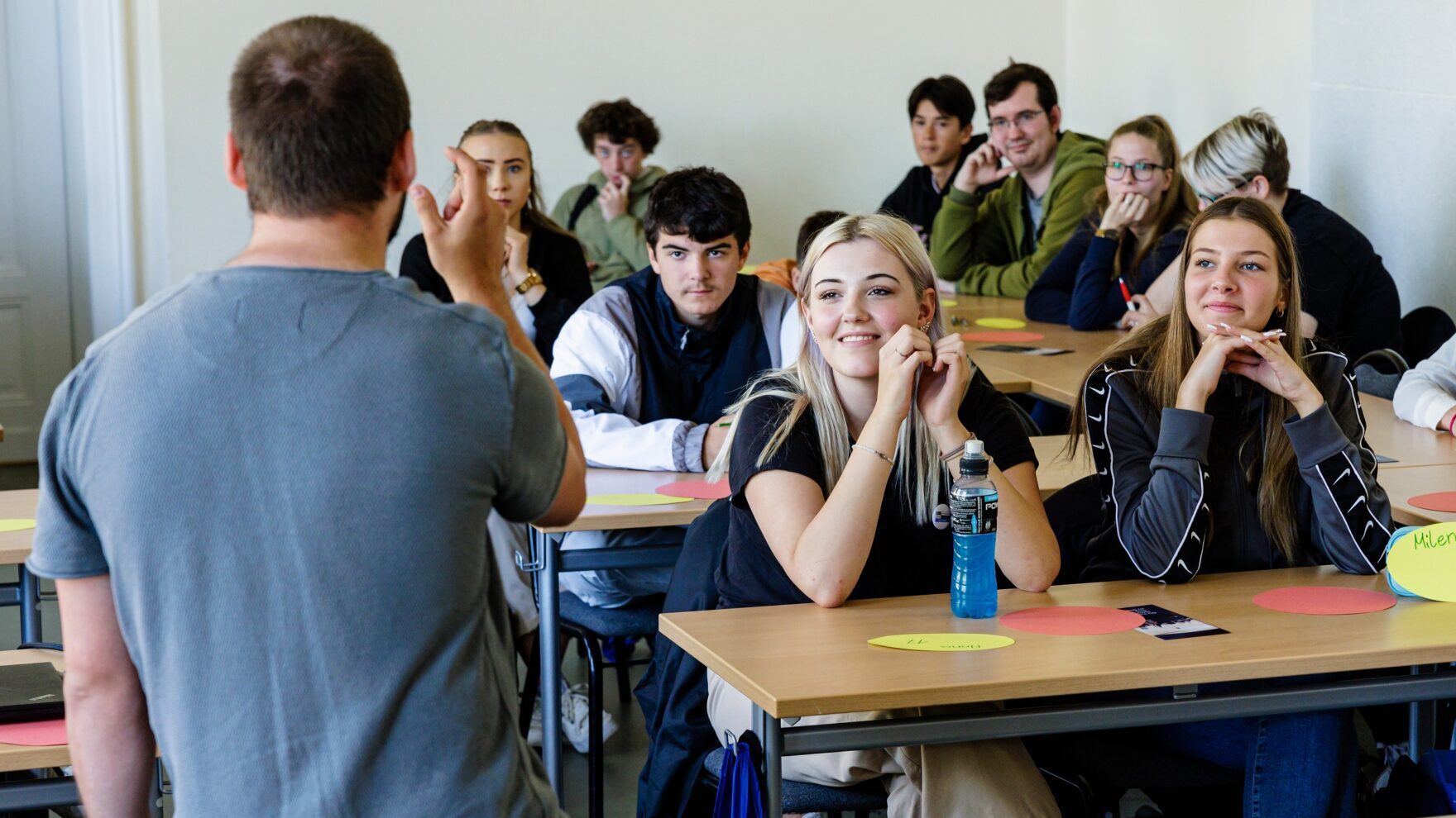 Auf dem Foto ist eine Schulklasse aus Sicht des Lehrer zu sehen. Auf den Tischen der Schüler*innen sind Workshopmaterialien.