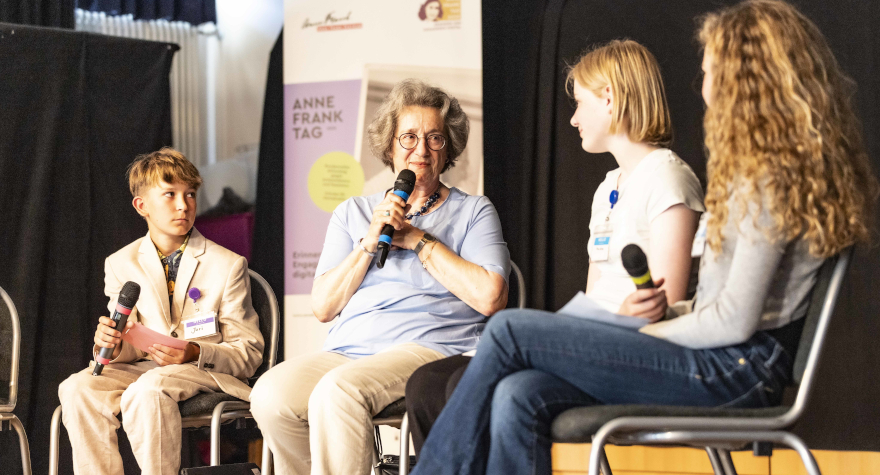Drei Schüler*innen interviewen eine ältere Dame auf der Bühne